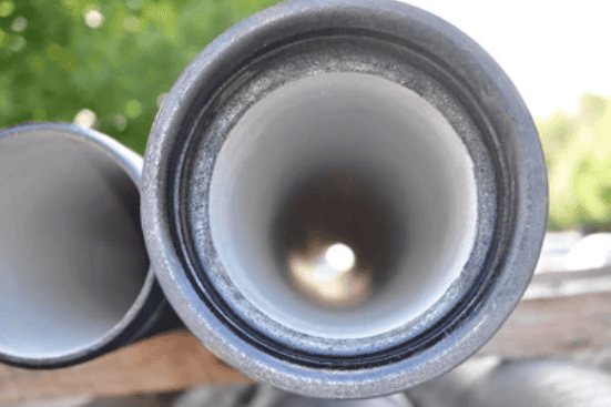 Close-up view of the ends of two large metal pipes, with the pipe on the left partially visible and the one on the right providing a clear perspective down its hollow interior, leading to a bright, out-of-focus background—indicative of our Reliable Appliance Installation Services.