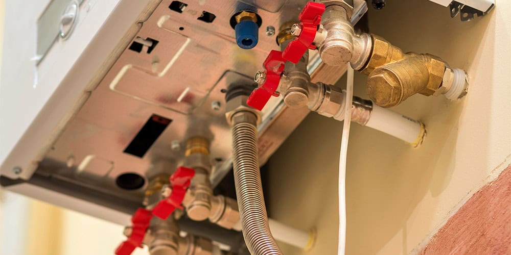 Close-up view of a plumbing system with various pipes and red valve handles connected to what appears to be a boiler or heating unit. The pipes, part of the hot water system inspection services, vary in size and material; some are metallic while others are plastic.