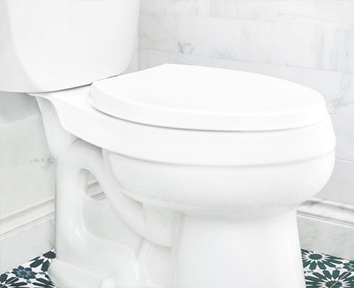 A white toilet with a closed lid is positioned against a tiled wall, showcasing the serene aesthetics that could distract from Common Plumbing Issues Homeowners Face. The floor displays patterned tiles in green and white, beautifully complementing the white wall tiles with their marble-like texture.