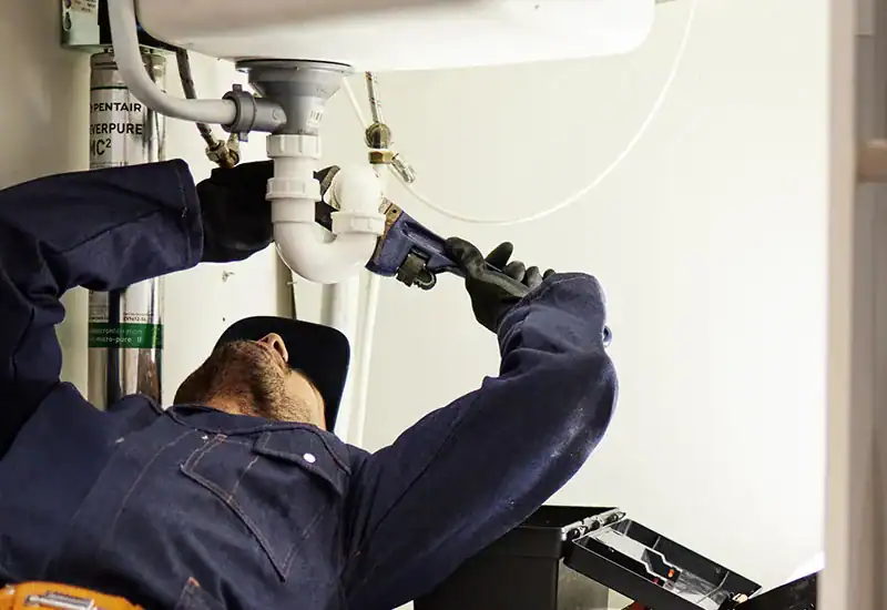 plumber under sink fixing leaking drain pipe